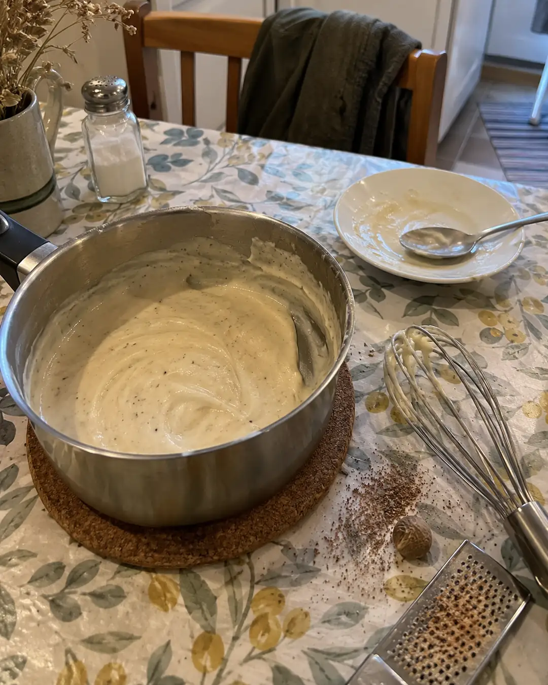 Kleiner Topf mit heller Béchamelsauce aus zuckerfreiem Haferdrink, daneben ein Schneebesen auf der Arbeitsplatte