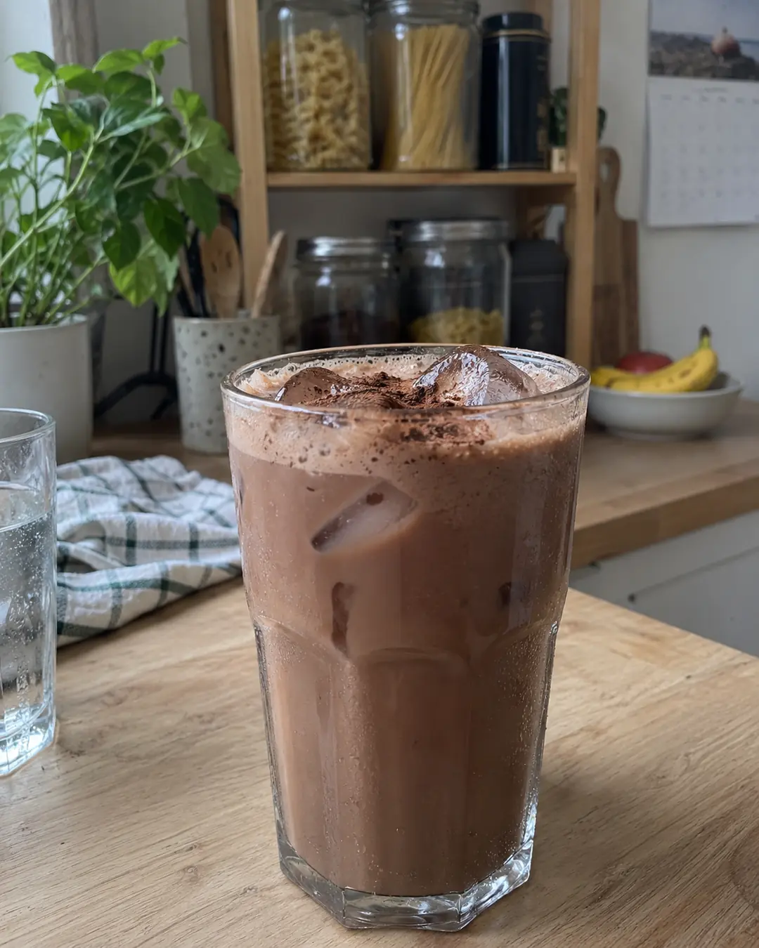 Glas kalte Schokomilch aus Haferdrink und Kakao mit Eiswürfeln und feinem Schaum